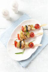Grilled shashliks with chicken, cherry tomatoes, onion and red pepper. Bright wooden background. Top view. Copy space.