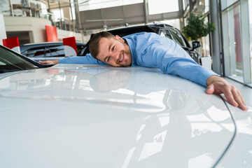 Handsome man hugging new car in dealership