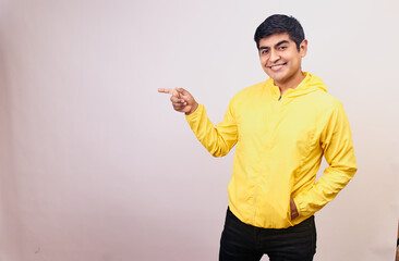 Hombre joven y feliz con una mascarilla señala con sus manos y dedos. Modelo aislado en fondo blanco con casaca amarilla