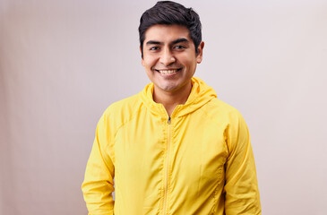 Hombre joven y feliz mira directo a la cámara. Modelo aislado en fondo blanco con casaca amarilla