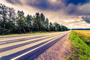 Highway passing near the field with haystacks. View from the roadside