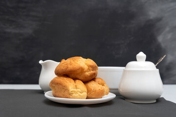 Homemade delicate profiteroles on table, cup of tea. Traditional French eclairs. Gray background