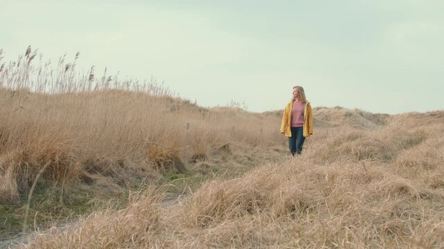 blond girl walking in dune landscape in yellow raincoat travel holiday