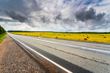 Highway passing near the field with haystacks. View from the roadside