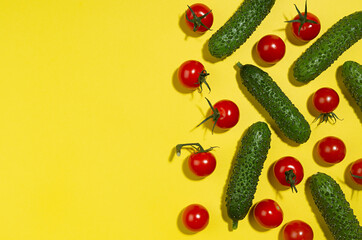Vegetable colorful abstract pattern - ripe cherry tomato, green young cucumber with shadow as border on yellow background, top view.