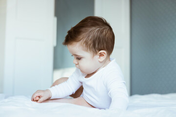 Portrait of toddler boy baby in white bodysuit on the bed in bedroom. Happy childhood concept