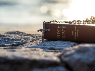 Close up crucifix pendant rosary and bible with bokeh blue sea morning light. Concept Love bible...