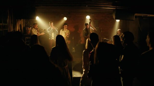 WIDE People dancing during concert of a modern jazz band playing on a stage of a small crowded venue. Shot with 2x anamorphic lens