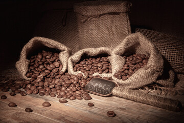 Vintage. Coffee beans in bags, scattered on a wooden table, illuminated by a beam of warm light. Spoon for coffee beans.