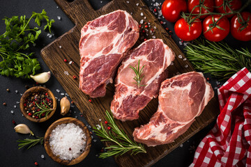 Pork meat, raw pork steaks on cutting board with ingredients for cooking. Top view with copy space.