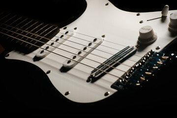 Close up picture of a black electric guitar on a black background.