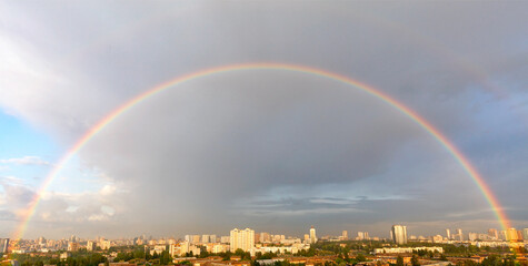 Large rainbow semicircle in the cityscape of the daytime sky.
