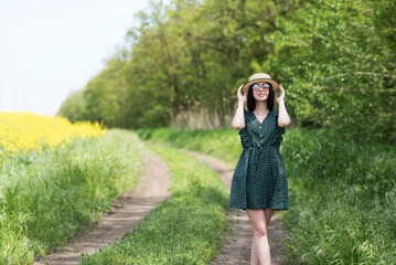 Obraz premium Portrait of a girl in a hat and a green dress in front of a rapeseed field.