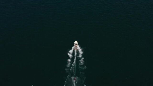 Top view of a white boat with a skier on a rope. Man water skiing moving behind the boat on the water.