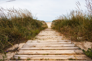 Obraz premium Wooden walkway extended on a fine sandy beach with the Mediterranean Sea in the background. In a cloudy sunset.
