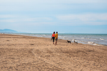 A couple walking and playing with two dogs on an empty beach. 