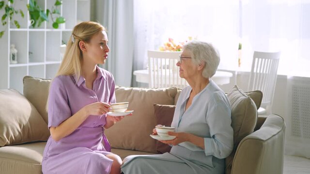 Talking young daughter and elderly mom with cups of tea