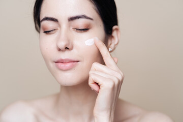 Close up beauty portrait of a laughing beautiful half naked woman applying face cream over beige background