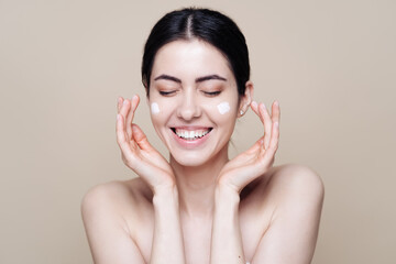 Close up beauty portrait of a laughing beautiful half naked woman applying face cream over beige background