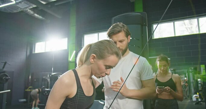 Trainer support. Athlete woman doing push ups with trx fitness straps in the gym while join lessons in sport club under the supervision of a coach. Workout and healthy lifestyle concept