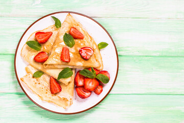 Crepes with srawberries and honey. Top view at wooden table.