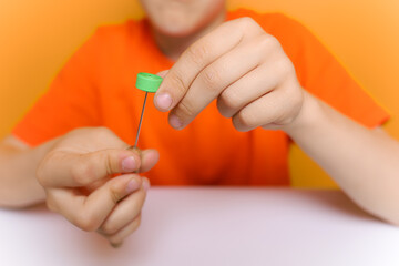the boy's hands in the foreground hold a quilling tool and thin colored strips of paper