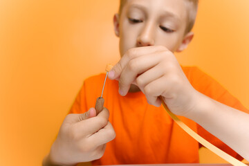 a child in an orange T-shirt tries to insert a thin strip of paper into a quilling tool