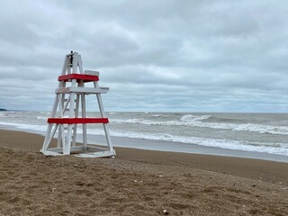 Empty lifeguard chair sits on a Lake Michigan beach on a stormy day as waves crash along the shore in the background. The beach is closed due to rough water and gale wind warnings.