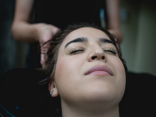 Hairdresser washing hair of a beautiful young adult woman in hair salon.