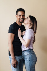 Naklejka premium Portrait of happy multiracial couple hugging and posing together over beige background in studio, romantic guy cuddling his afro girlfriend