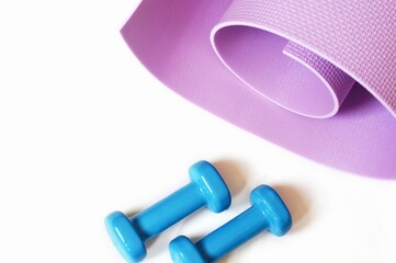 Top view workout equipment on a white background. Rolled purple mat and blue dumbbells. Fitness, sport concept, healthy lifestyle