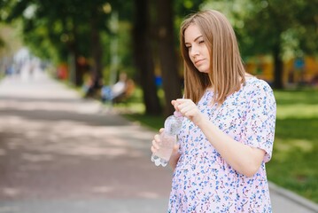 Pregnant woman stands in the park with a bottle of water. copy space