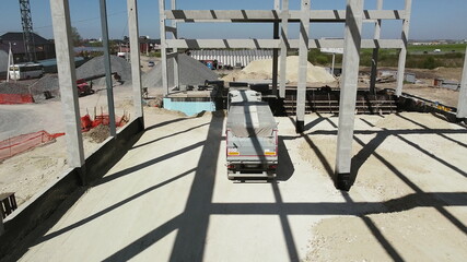 Truck travels on the territory of new construction. Reinforced concrete frame of the new building. A truck with a covered trailer brought sand or soil to the construction site. Delivery of Material