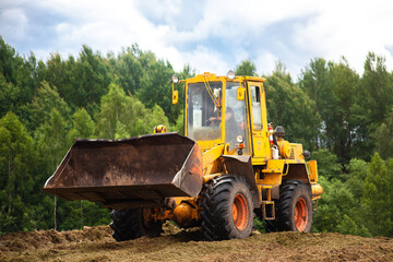 Obraz na płótnie Canvas A yellow bulldozer is compacting a green mass of cut grass. 