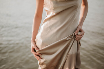 silhouette of a woman in a silk golden dress against the background of river water, beautiful folds...