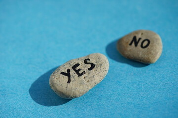 Obraz na płótnie Canvas Two pebbles with the text yes and no on a blue table