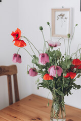Beautiful poppies bouquet on wooden table in room. Gathering countryside wildflowers, rural still life. Red common poppy and purple opium poppy flowers in vase