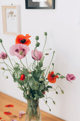 Beautiful poppies bouquet on wooden table in room. Gathering countryside wildflowers, rural still life. Red common poppy and purple opium poppy flowers in vase