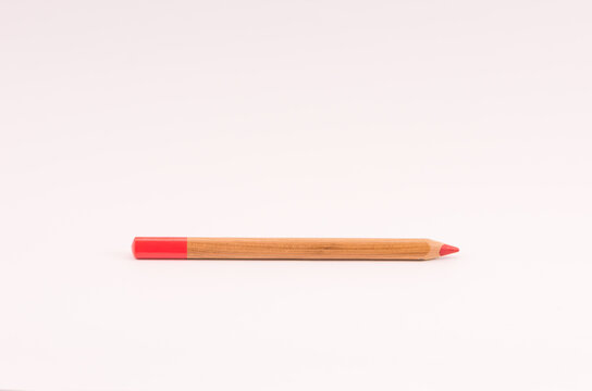 Closeup of a wooden red pencil on light opink empty surface