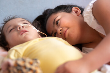 child with physical disability sleeping and sister looking at her.