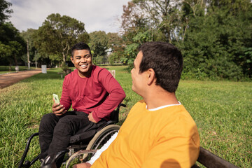 person in wheelchair laughing and talking to friend in park.