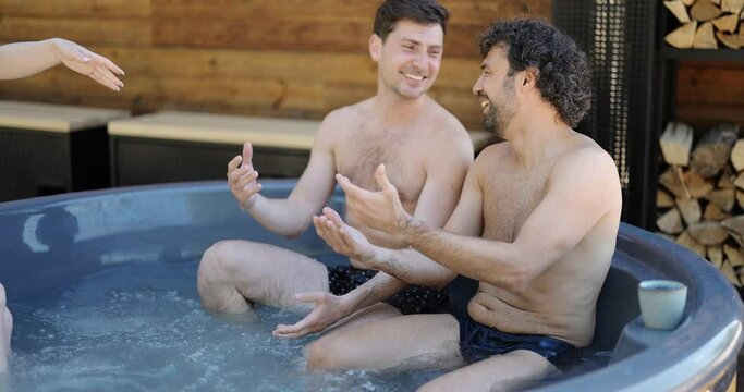 Company of friends bathing in outdoor jacuzzi or hot vat near the spa and lake. Couples have fun and relax in wellness center