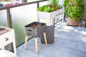 A vermicomposting system (worm composter) sits on an apartment balcony with other patio planters. Worms eat food scraps and produce worm castings and worm tea to be used as fertilizer. Redirect waste. - obrazy, fototapety, plakaty