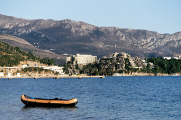 Fototapeta na wymiar Inflatable boat on the sea against the backdrop of the coast with houses, green trees and mountains