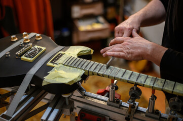 Master guitar luthier hands polishes the frets on the fretboard