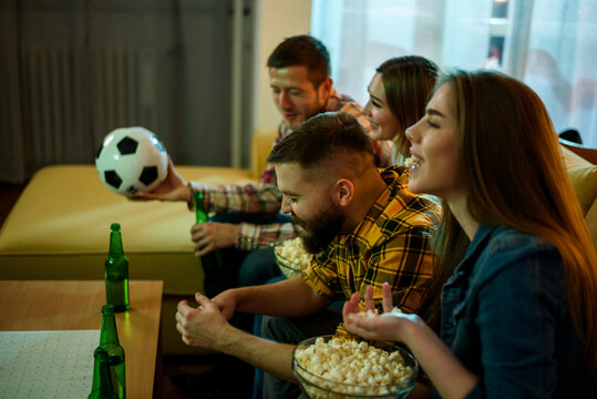A group of friends watching football game at home and drinking beer