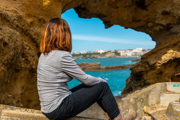 A young woman looking in a window on the rocks next to Plage du Port Vieux in Biarritz, on vacation in southeastern France. Biarritz, department of Pyrenees-Atlantiques