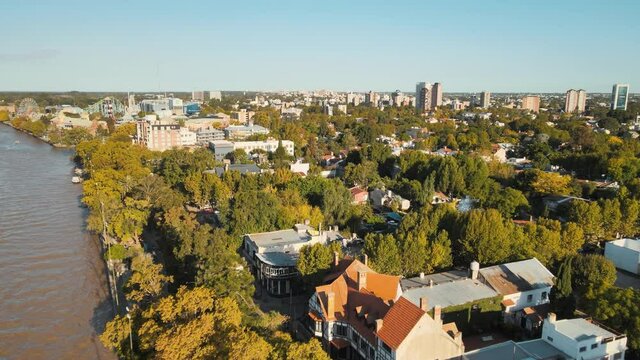 Aerial dolly in over Tigre houses and trees with amusement park in background beside de la Plata River, Buenos Aires