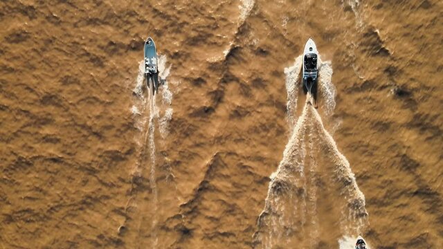 Aerial top down of a group of yachts sailing on a brown color river at daytime
