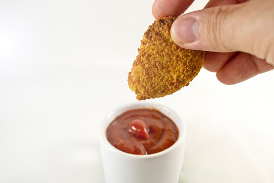 Isolated Hand Dipping A Chicken Nugget Into A Small Ketchup Cup, With A White Background.